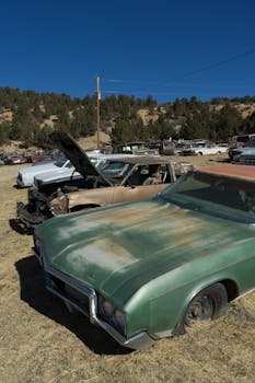 Rusty vintage cars in an outdoor Nevada City scrapyard under a clear blue sky.